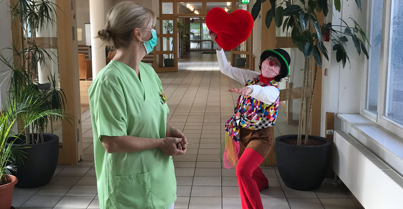 Humor in der Pflege – für die seelische Gesundheit: Pflegerin und Clown mit Herzkissen