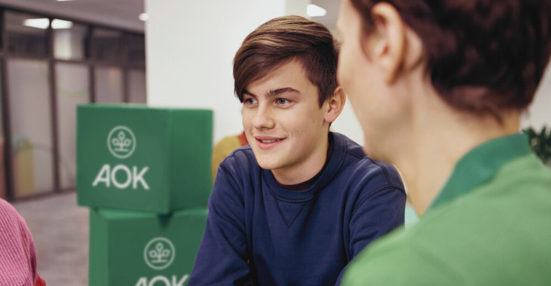 Azubi-Gesundheitstag: Männlicher Jugendlicher im Gespräch mit AOK-Mitarbeitenden während des Azubi-Gesundheitstags