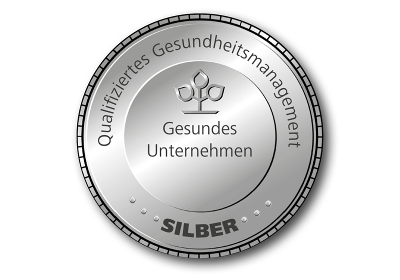 Gesundes Unternehmen: Das Siegel für qualifiziertes Gesundheitsmanagement in Silber Silberfarbendes, rundes Siegel auf dem „Gesundes Unternehmen, Qualifiziertes Gesundheitsmanagement“ und „Silber“ steht.