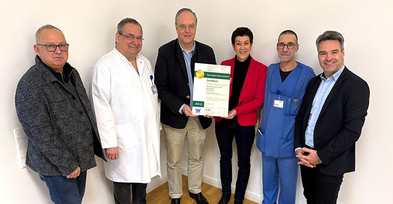 Zu sehen sind fünf Männer und eine Frau. Zwei davon halten das Gold Zertifikat in der Hand.