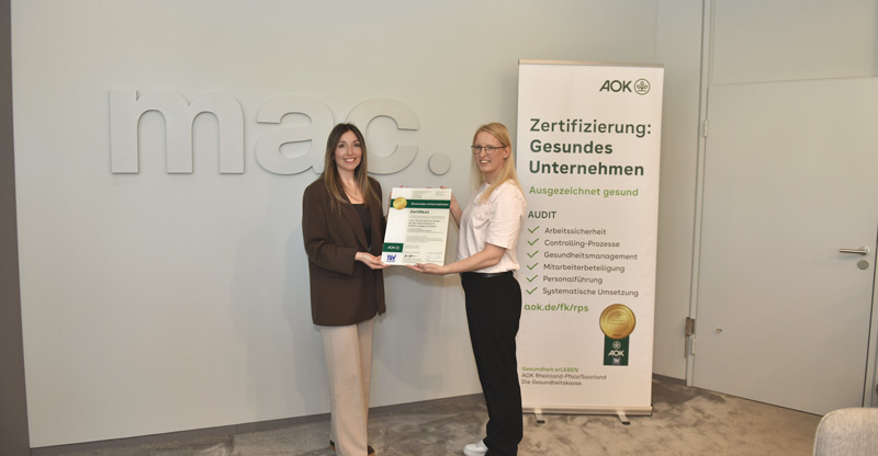 mac. brand spaces GmbH Zwei Frauen stehen vor einem Banner der AOK und beide halten ein Zertifikat in der Hand