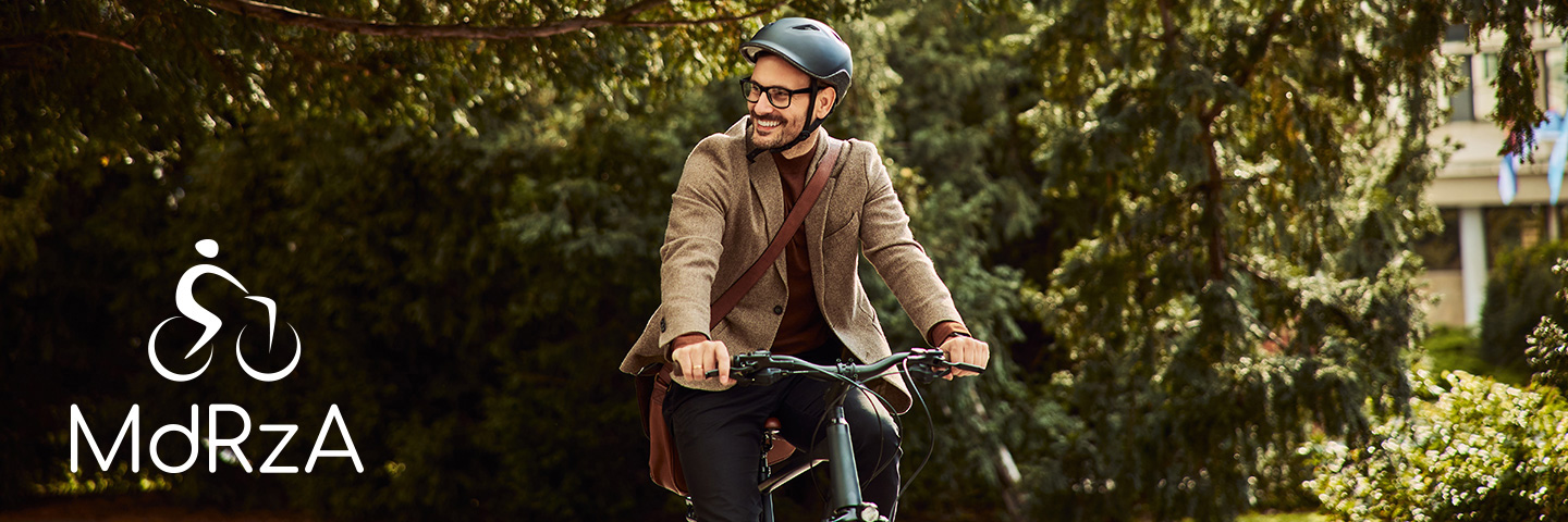 Mann mit Fahrradhelm fährt Fahrrad unter Bäumen vor einem Bürogebäude.