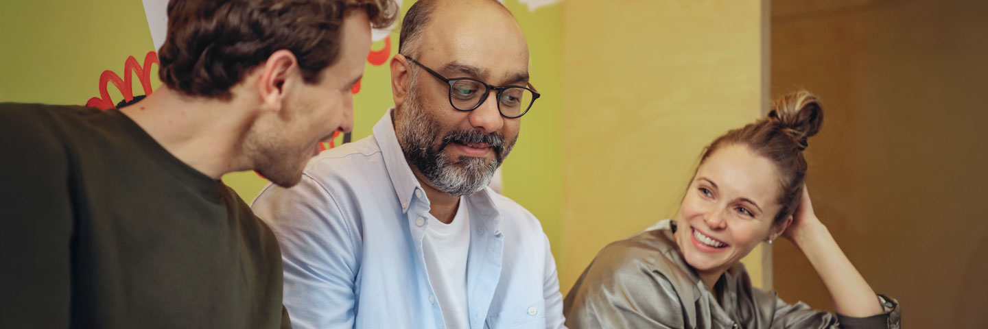 Diversität im Unternehmen: Drei Teammitglieder im freundlichen Austausch Diversität im Unternehmen: Drei Teammitglieder im freundlichen Austausch