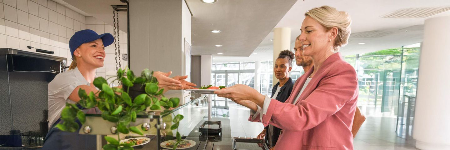 Nachhaltige Ernährung bei der Arbeit: Eine Frau nimmt an der Salatbar der Kantine einen Teller entgegen