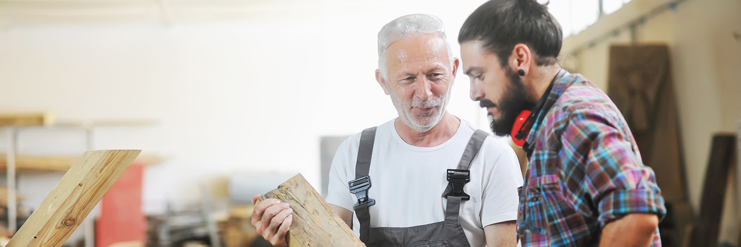 Der demografische Wandel ist für viele Unternehmen eine große Herausforderung Ein älterer Arbeitnehmer erklärt einem junger Arbeitnehmer etwas