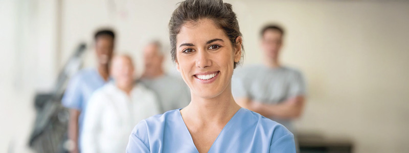 Pflegekräfte stärken: Eine Pflegekraft lächelt Betrachtende an, hinter ihr stehen weitere Mitarbeitende. 
