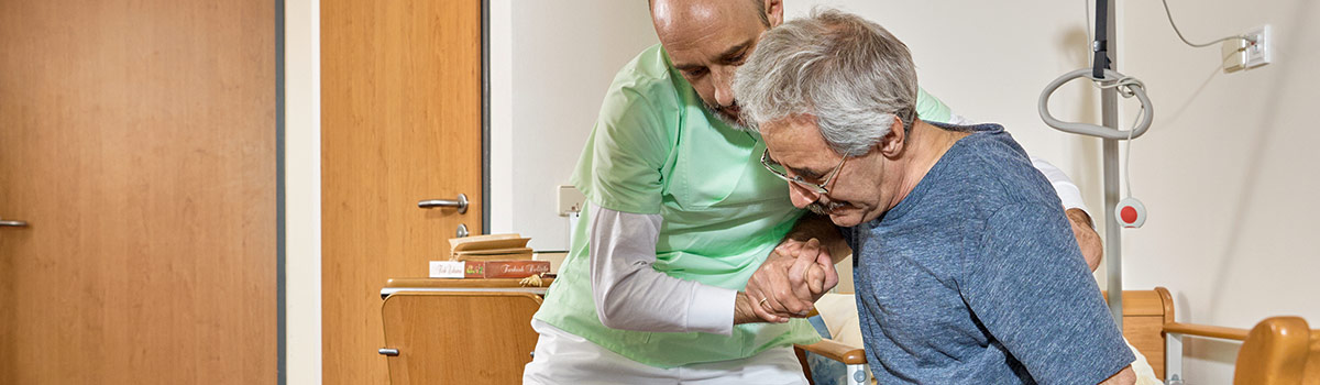 Ein Pfleger hilft einem Patienten aus dem Bett.