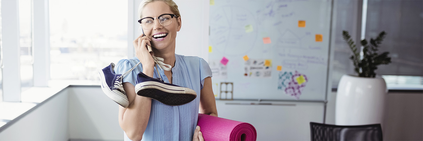 Betriebliche Gesundheitsförderung verbessert auch die Unternehmenskultur Eine lachende Frau steht telefonierend in einem Yoga studio