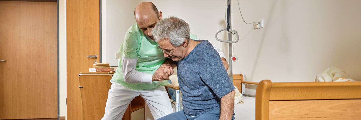 Ein Pfleger hilft einem Patienten aus dem Bett.