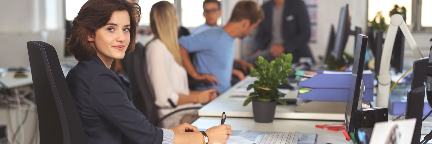 Eine Gruppe Mitarbeitende im Büro sitzt an Schreibtischen.