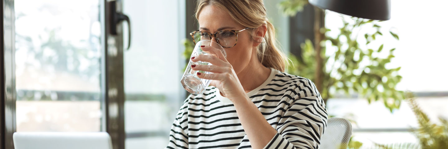 Eine Frau sitzt am Tisch und trinkt Wasser aus einem Glas.