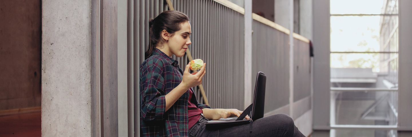Eine junge Frau sitz mit einem Snack in der Hand im Flur und lächelt