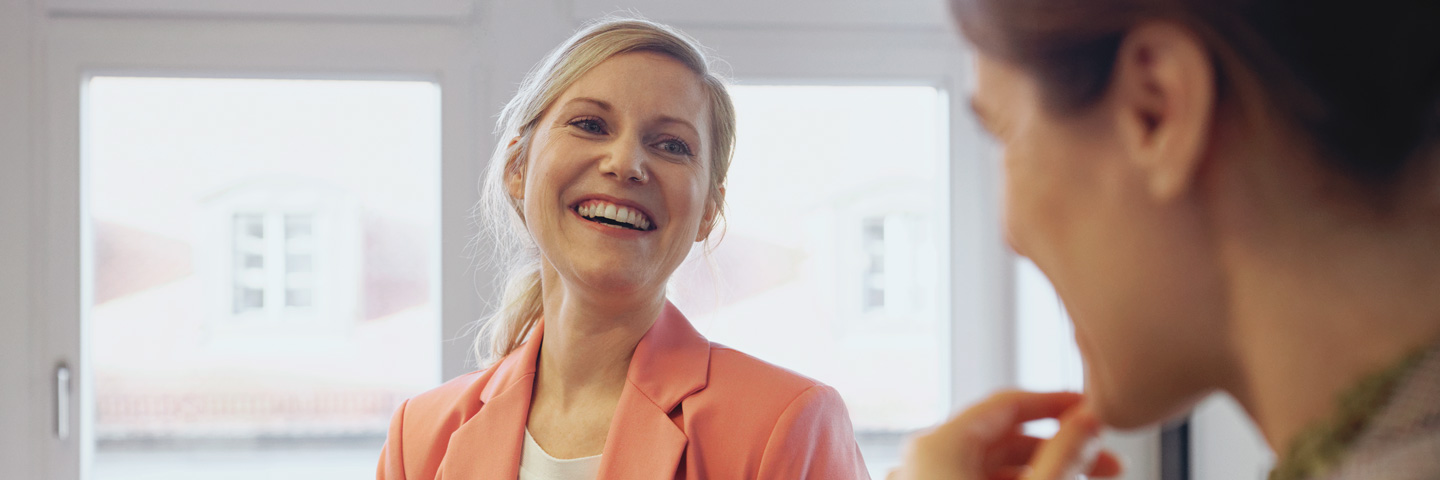 Eine Frau im Büro lacht ihren Kollegen an.