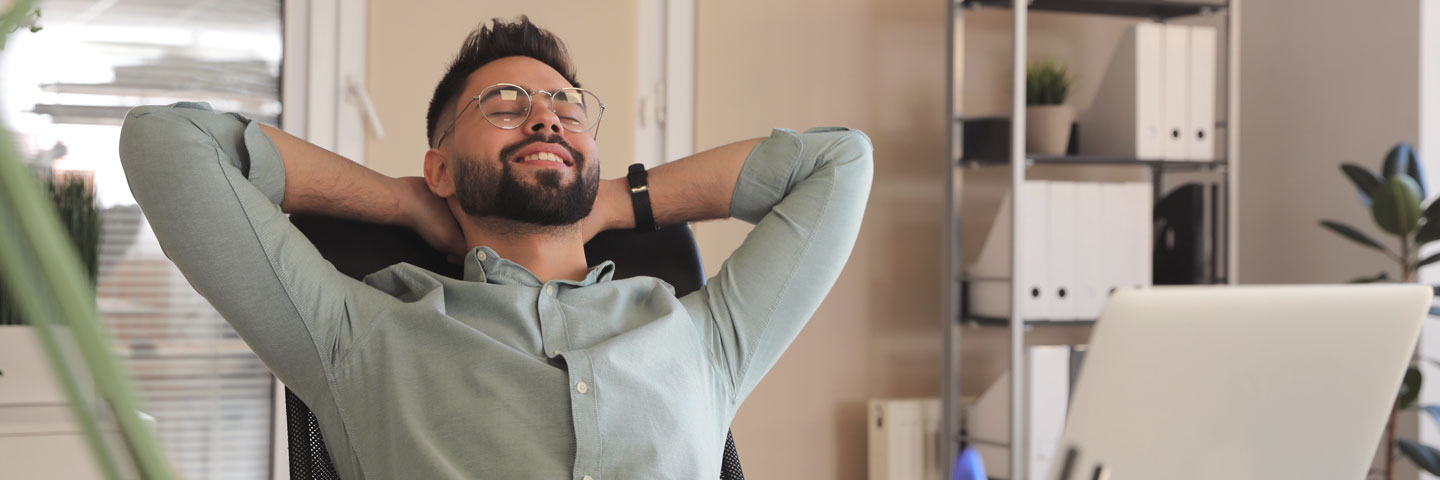 Mann im Büro lehnt sich entspannt zurück und hat lächelnd die Augen geschlossen