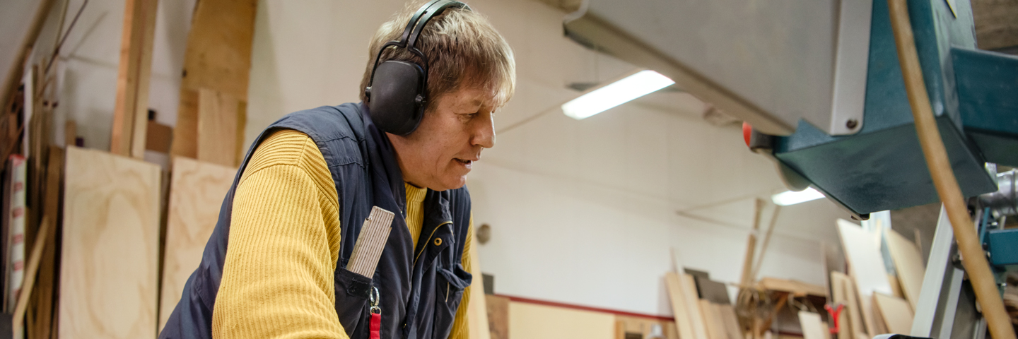 Mann steht mit Kopfhörern an einem Gerät in einer Schreinerwerkstatt