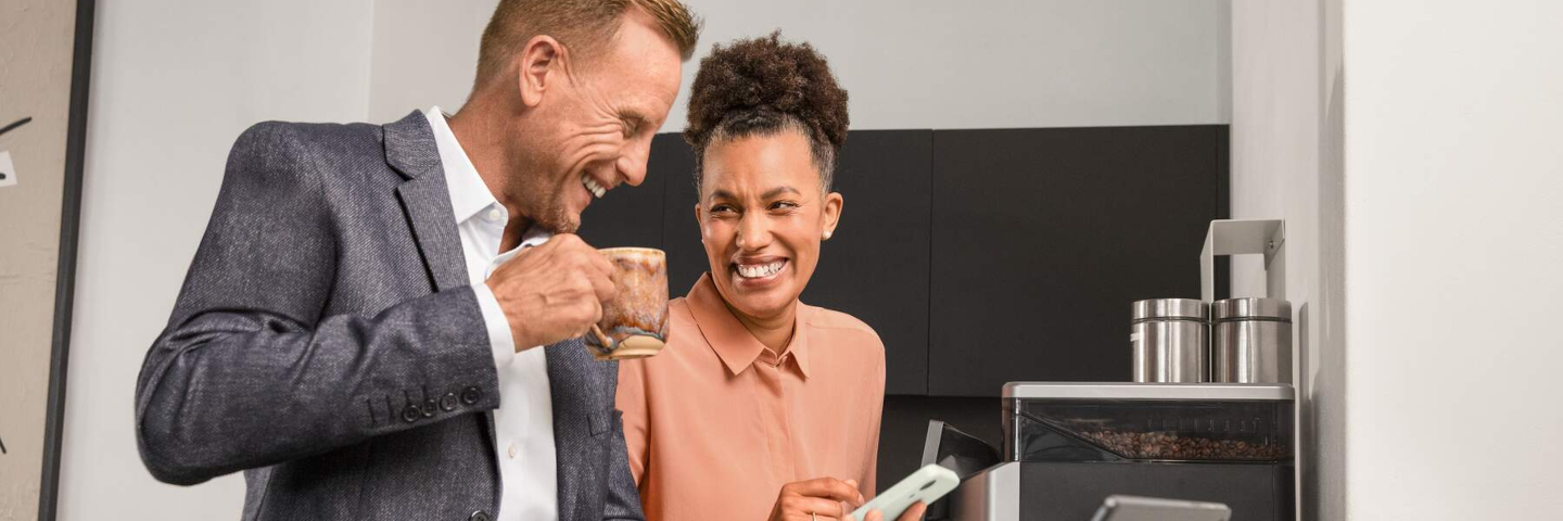 AOK atWork: Zwei Menschen schauen in einer Büroküche gemeinsam auf ein Smartphone AOK atWork: Zwei Menschen schauen in einer Büroküche gemeinsam auf ein Smartphone