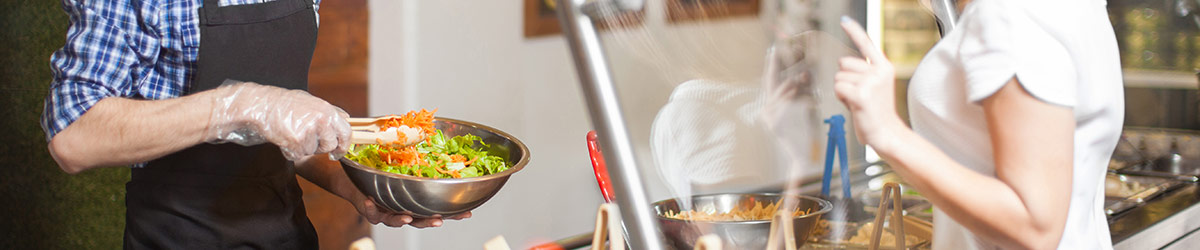 Eine Frau wählt in der Kantine Salat aus.