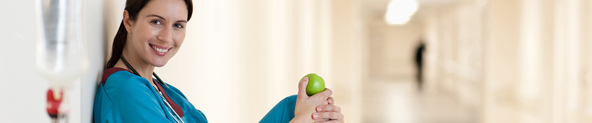 Junge Frau in Arztkittel isst einen Apfel