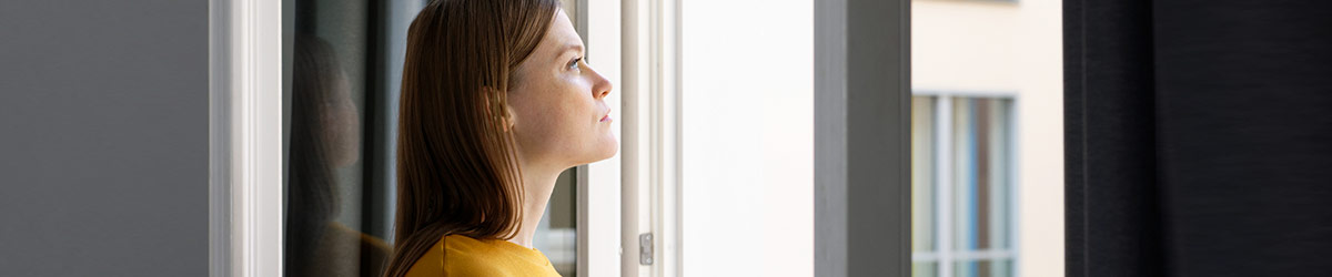 Eine junge Frau starrt aus dem Fenster ihrer Wohnung.