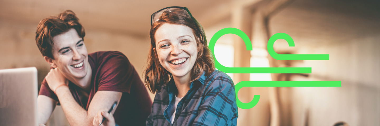 Zwei lächelnde Auszubildende in einer Werkstatt-Umgebung mit eingeblendetem grünen Grafik-Symbol.