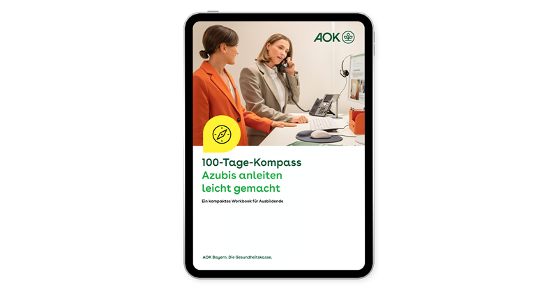 AOK-100-Tage-Kompass Das Titelblatt des AOK-100-Tage-Kompasses zeigt zwei Frauen, die in einem Büro an einem Schreibtisch stehen, während eine telefoniert und die andere zuschaut.