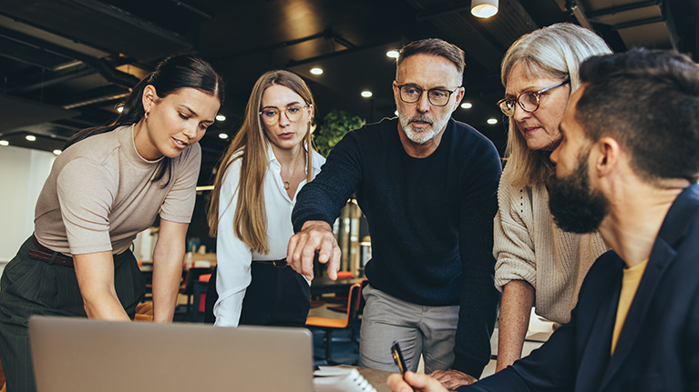 Online-Seminare Eine Gruppe von Menschen steht im Büro und sieht sich Inhalte auf einem Rechner an.