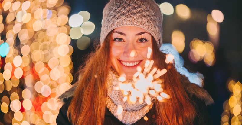 Neuerungen zum Jahreswechsel Junge Frau mit Mütze und Schal hält lächelnd eine brennende Wunderkerze.