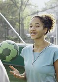 Boost your Basics: fit im Job Lachende junge Frau wirft auf einem Sportplatz im Freien einen Ball in die Luft.