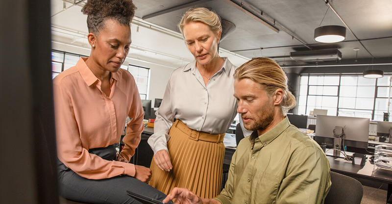 Interkulturelle Zusammenarbeit: Drei Kolleginnen und Kollegen besprechen gemeinsam Inhalte auf einem Tablet in einem modernen Großraumbüro. Interkulturelle Zusammenarbeit: Drei Kolleginnen und Kollegen besprechen gemeinsam Inhalte auf einem Tablet in einem modernen Großraumbüro.