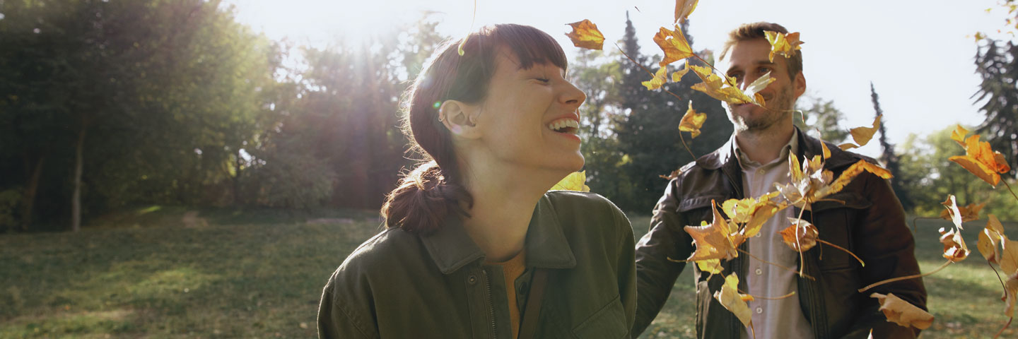 AOK-Mitglied werden: Eine Frau und ein Mann an einem sonnigen Herbsttag im Park, umgeben von Laub