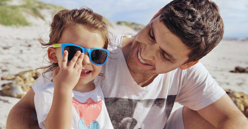 AOK-Mitglied werden: Mann sitzt mit Kind am Strand AOK-Mitglied werden: Mann sitzt mit Kind am Strand