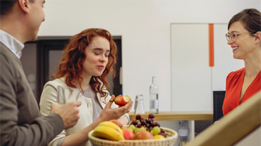 Mitarbeitende stehen ein Obst essend um einen Obstkorb herum.