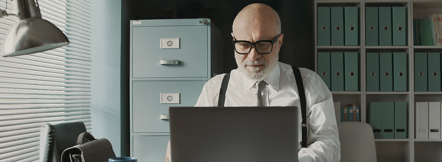 Ein älterer Mann sitzt im Büro und liest den neuen AOK-Newsletter an seinem Laptop.