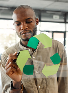 Ein Mann steht vor einer Glaswand und malt ein Recyclingsymbol darauf
