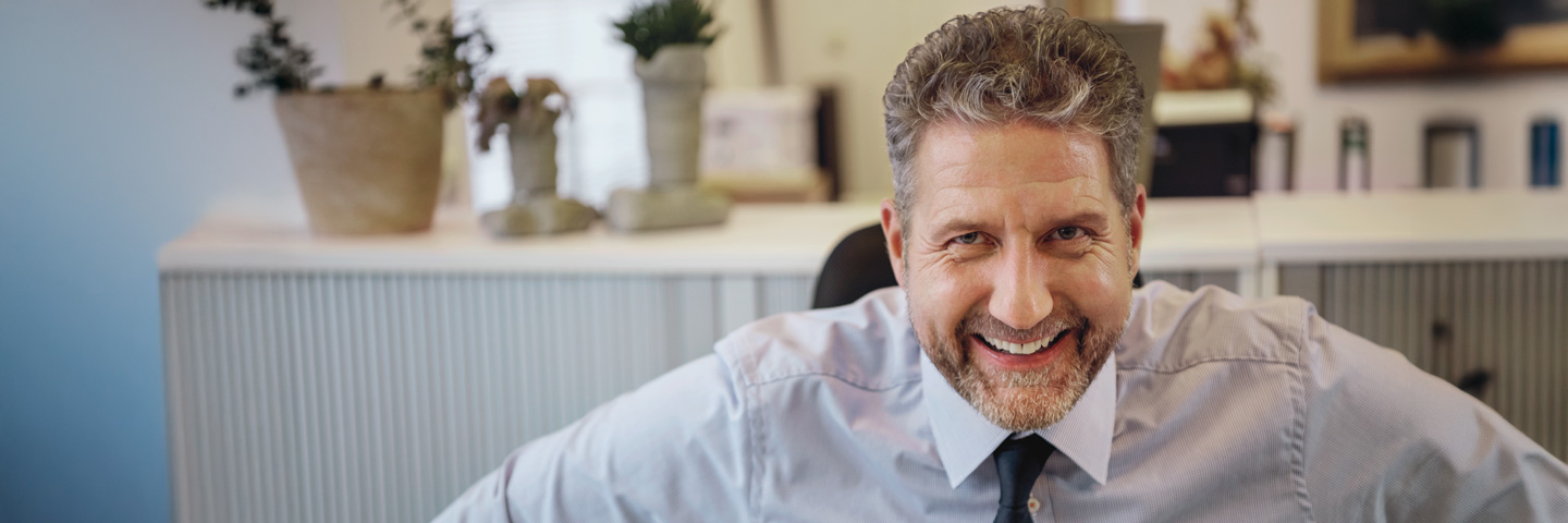 Ein Mann im Büro schaut lachend über seinen Bildschirm. Immer informiert mit dem AOK-Magazin für Arbeitgeber.