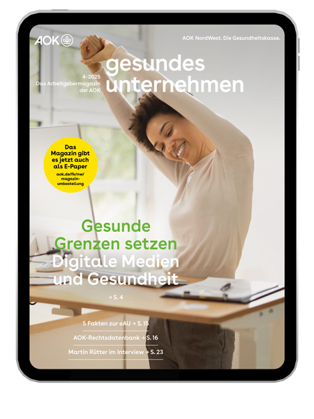 gesundes unternehmen Ausgabe 4-2025: Eine am Schreibtisch stehende Frau streckt sich gut gelaunt