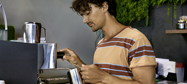 Aushilfen: höhere Grenzwerte für die Lohnsteuerpauschalierung Ein junger Mann schäumt an einer professionellen Kaffeemaschine Milch auf.