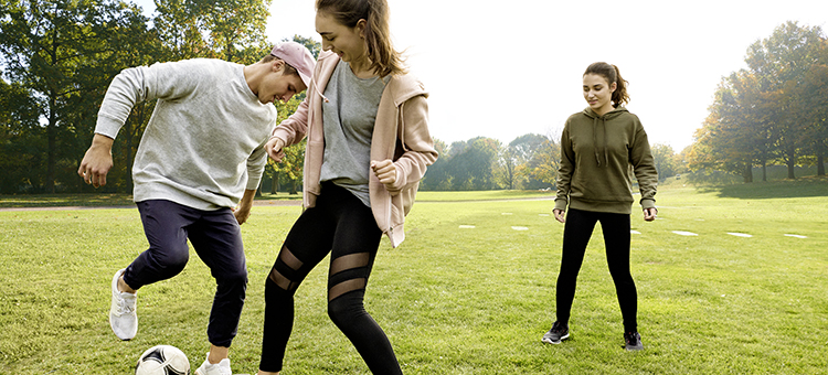 Gemeinsam Sport zu treiben, verbessert das Betriebsklima. Drei junge Auszubildende spielen Fußball im Freien.
