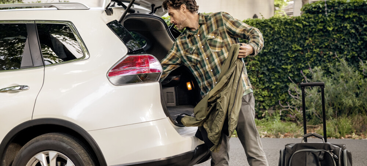 Rechtliche Beurteilung von Entsendungen ins Ausland. Ein Mann räumt seinen Kofferaum aus und nimmt eine Jacke heraus. Der Koffer steht vor dem Auto.