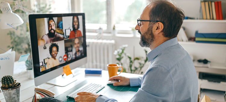 Der Teamgeist lässt sich auch im Homeoffice stärken. Ein Mann nimmt zu Hause an einer virtuellen Konferenz teil.