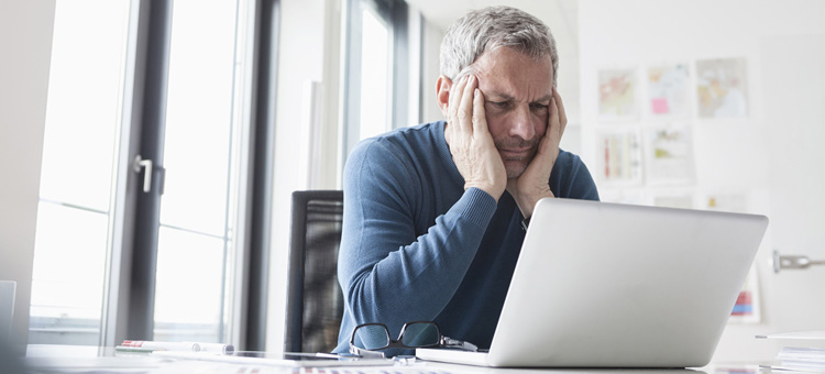 Digitalen Stress reduzieren Ein Beschäftigter sitzt mit müdem Gesichtsausdruck am Rechner.