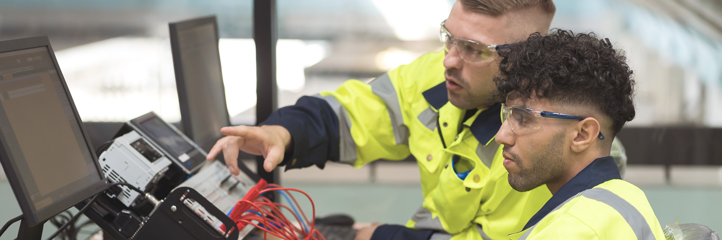 Studierende aus dem Ausland: Zwei Männer in Schutzausrüstung arbeiten am Computer.