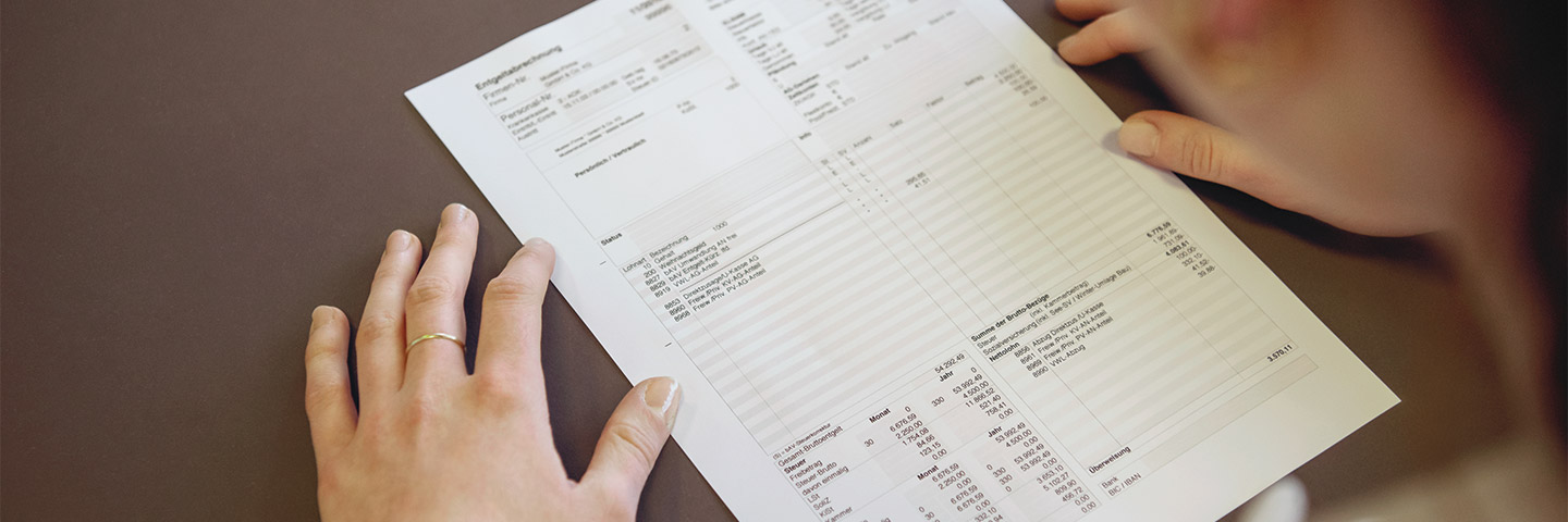 Berechnung der Gesamtsozialversicherungsbeiträge bei Einmalzahlung: Eine Frau beugt sich über eine ausgedruckte Gehaltsabrechnung. Berechnung der Gesamtsozialversicherungsbeiträge bei Einmalzahlung: Eine Frau beugt sich über eine ausgedruckte Gehaltsabrechnung.