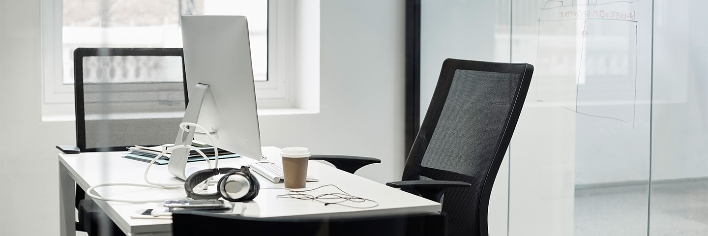 Absentismus erkennen: helles, leeres Büro mit Schreibtisch, Computer, Kopfhörern und Kaffeebecher.