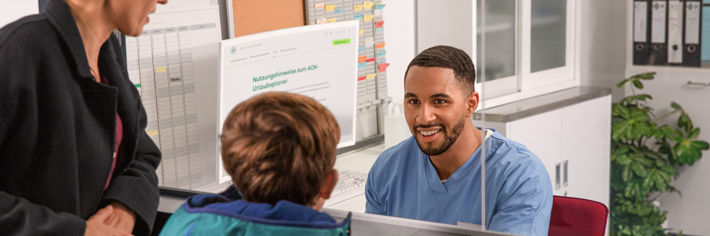 Überstunden und Wochenendarbeit im SV-Recht: Mann in medizinischer Arbeitskleidung spricht mit einer Frau und einem Kind an einem Empfangstresen.
