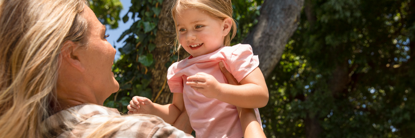Familienfreundlichkeit in Unternehmen: Eine Frau hebt ein Kind im Park hoch, während ein Mann danebensteht.