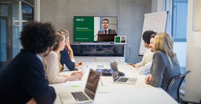 Teilnehmende eines Trends & Tipps Online-Seminars sitzen an einem Tisch und schauen sich die Präsentation an. 