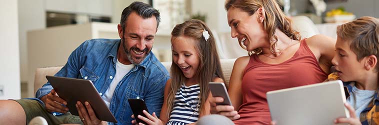 Familie mit Tablets und Smartphones sitzt auf dem Sofa und schaut auf das Handy der Tochter.