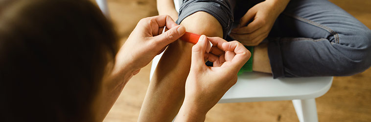 Online-Seminar „Erste Hilfe für Kinder“ Eine Mutter klebt ihrem Kind ein kleines Pflaster auf das geschrammte Knie.