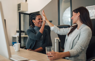 Zwei Frauen klatschen „Highfive“ am Schreibtisch sitzend